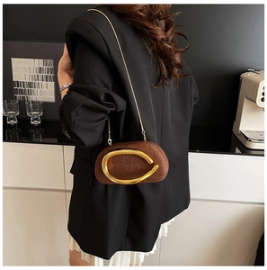 Close-up of brown textured crossbody bag with oversized gold ring buckle and chain strap