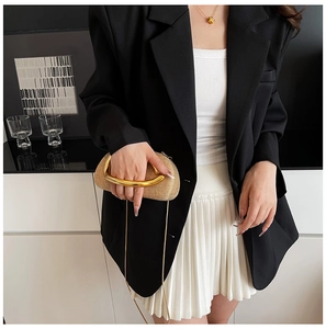 Detail of beige straw clutch bag with oval gold handle and crossbody metal chain strap