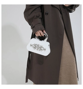 Close-up of white evening box bag featuring shimmering rhinestones and a silver U-shaped handle