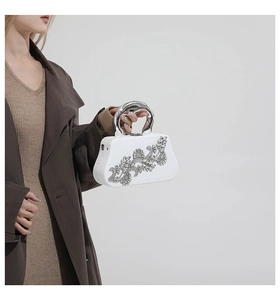 Close-up of white evening clutch with crystal floral motifs and silver metal handle