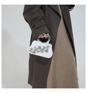 Close-up of white evening clutch with crystal flower pattern and silver ring handle