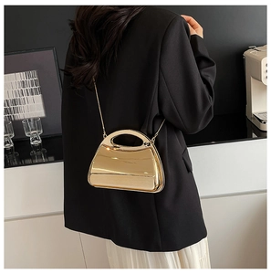 Detail of a gold metallic hard shell handbag featuring a sleek trapezoid shape and chain strap