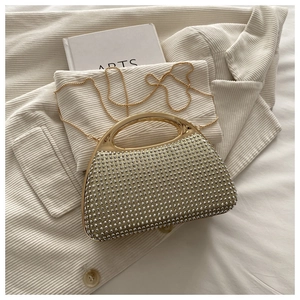 Close-up of sparkling silver rhinestone handbag with golden handle on white fabric