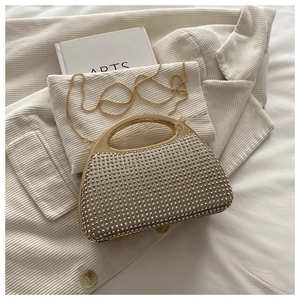 Detail of shimmering gold evening bag with rhinestones and metal handle on white jacket