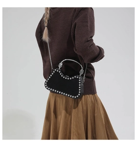 Detail view of a black velvet handbag with silver studs and a carved metal handle on model