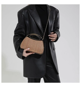 Detailaufnahme einer gewebten Strohhandtasche mit Metallgriff und Kette auf schwarzem Blazer