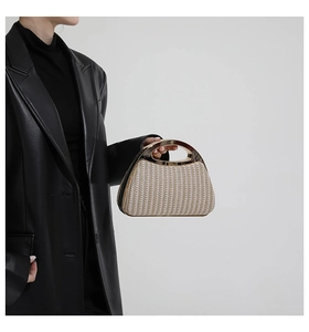 Detail der gewebten Strohhandtasche mit Goldmetallgriff auf schwarzem Leder-Outfit