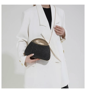 Schwarze Abend-Clutch mit goldenem Griff auf weißem Blazer-Hintergrund präsentiert