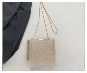 Close-up of champagne gold glitter clutch bag showing compact size next to a smartphone