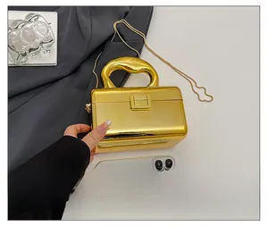 Detailed scale view of a gold mirror acrylic clutch box bag next to a smartphone