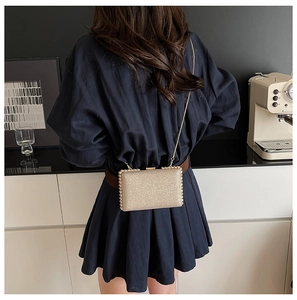 Detail of glittery gold mini square bag with golden chain shown in a lifestyle setting