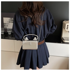 Silver metallic box clutch with lion head relief handle on a blue pleated dress