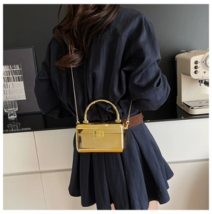 Mini gold mirror acrylic box bag with metallic handle and chain on a blue dress