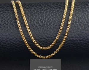 Close-up of a glossy golden stainless steel box chain necklace on black leather display