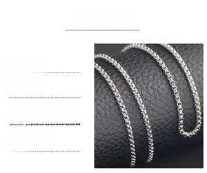 Detail of silver titanium steel box chain necklace on black textured surface