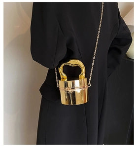 Detail of a shiny gold cylinder bag featuring a metallic handle and a slim chain strap