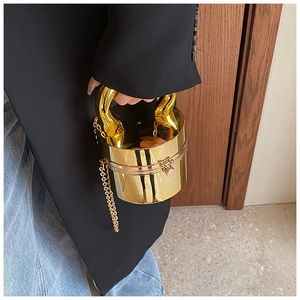 Detail of a shiny gold cylindrical acrylic box bag with metal handles and chain strap