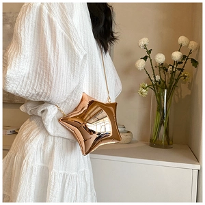 Model wearing a rose gold star-shaped chain bag with shiny metallic finish on white dress