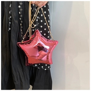 Close-up of a metallic pink star-shaped handbag with a gold chain strap held by a model