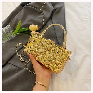 Close-up of golden box clutch with hammered metal texture and elegant curved handle
