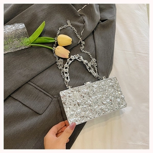 Detail of silver box clutch with wavy texture and dual chain on a grey blazer