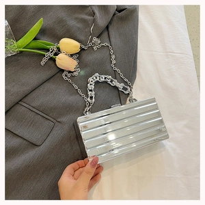 Detailed view of a silver metallic striped box bag with chunky chain handle on grey fabric