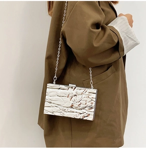 Detaillierte Makroaufnahme einer silbernen Metallic-Clutch mit Faltenstruktur und Kettenriemen