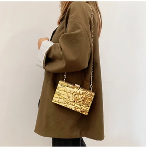 Detail der goldfarbenen Abendtasche mit Steppoptik, Metallic-Textur und feiner Kette