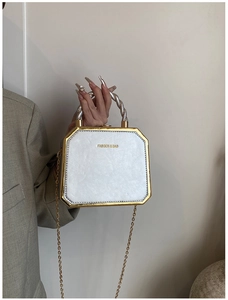 Detail of octagonal white faux leather bag with silver twisted handle and gold metal frame