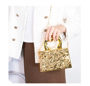 Dettaglio della borsa clutch dorata in acrilico con trama metallo liquido e catena
