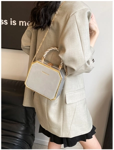Detail of silver box handbag with gold metal trim and twisted handle worn by model