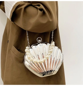 Detail of silver shell-shaped evening bag with pearl handle and metal chain on model