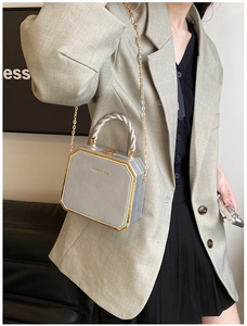 Detail of light gray hexagonal bag with gold metal handle and logo, worn with a green blazer