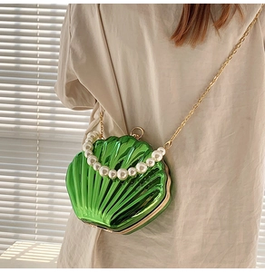 Detail of green shell-shaped purse featuring pearl handle and gold chain strap