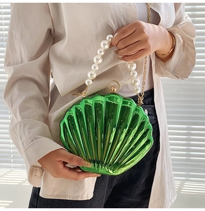 Detail of metallic green shell bag featuring large pearl handle and gold chain strap