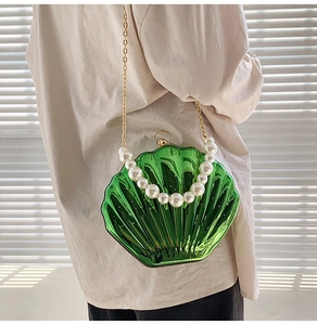 Detail of green shell bag with large faux pearl handle and gold chain strap on model