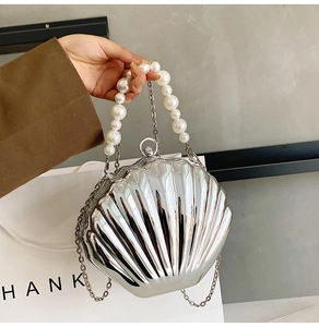 Detail of silver shell-shaped evening clutch bag with pearl handle and metal chain strap