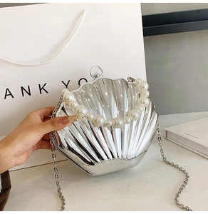 Detail view of silver shell-shaped clutch with large pearl handle and metal chain strap