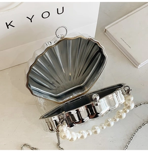 Detail of silver shell-shaped clutch featuring a pearl handle and metal chain strap