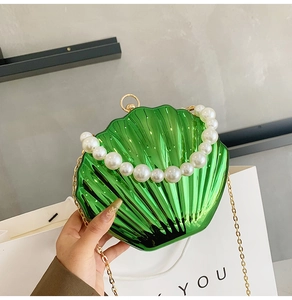 Detail of green shell-shaped clutch bag with pearl handle and golden chain strap