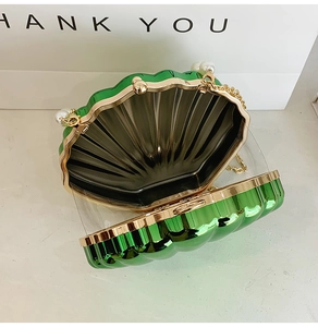 Detailed macro view of open green shell bag with golden metal frame and pearl accent