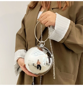 Silver spherical clutch bag with metal ring handle and chain strap on a green blazer