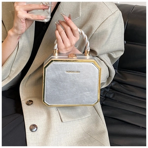 Detail of silver square handbag featuring golden hardware and woven twist handle