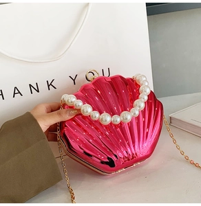 Detail of pink metallic shell-shaped clutch with large pearl handle and gold chain strap