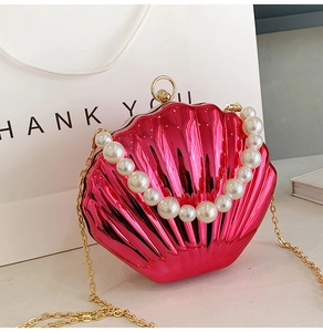 Detail of rose red shell bag featuring large pearl handle and shiny metallic finish