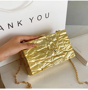 Makro-Detail der goldenen Stepp-Clutch mit Metallic-Textur und dünnem Kettenriemen