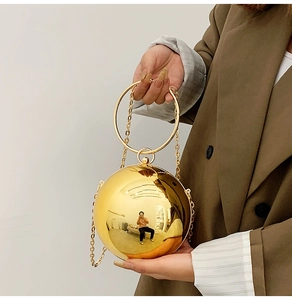 Detail of a spherical gold evening clutch bag with round metal handle and chain strap