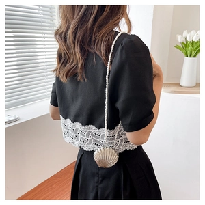 Detail of shell-shaped metallic crossbody bag with elegant pearl chain strap on model