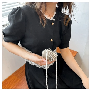 Close-up of a silver shell-shaped mini bag with a pearl chain strap on a black dress