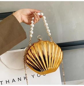 Detail of a gold shell shaped clutch bag featuring a large pearl handle and metallic texture